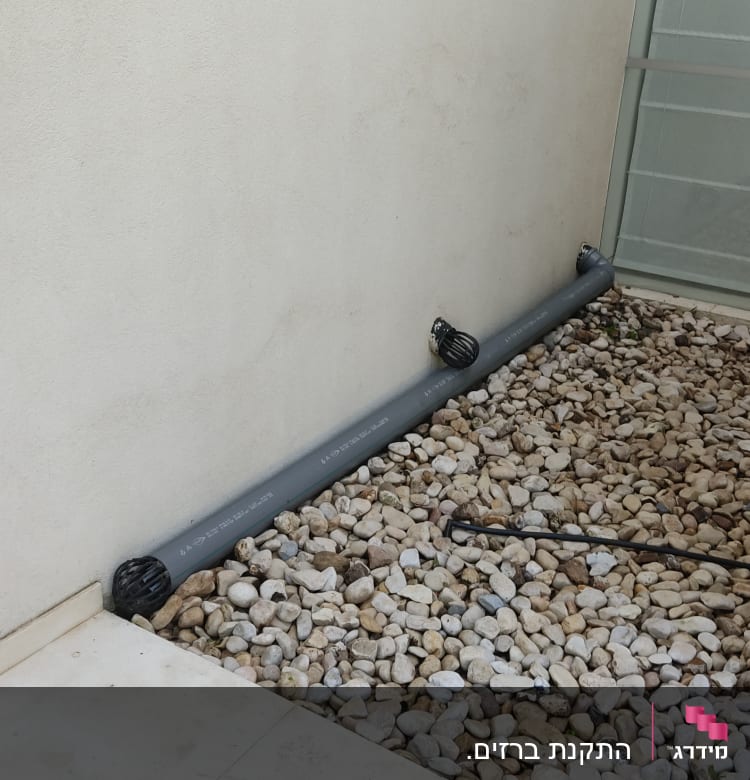 צינור אפור עם מכסים שחורים על אבנים קטנות